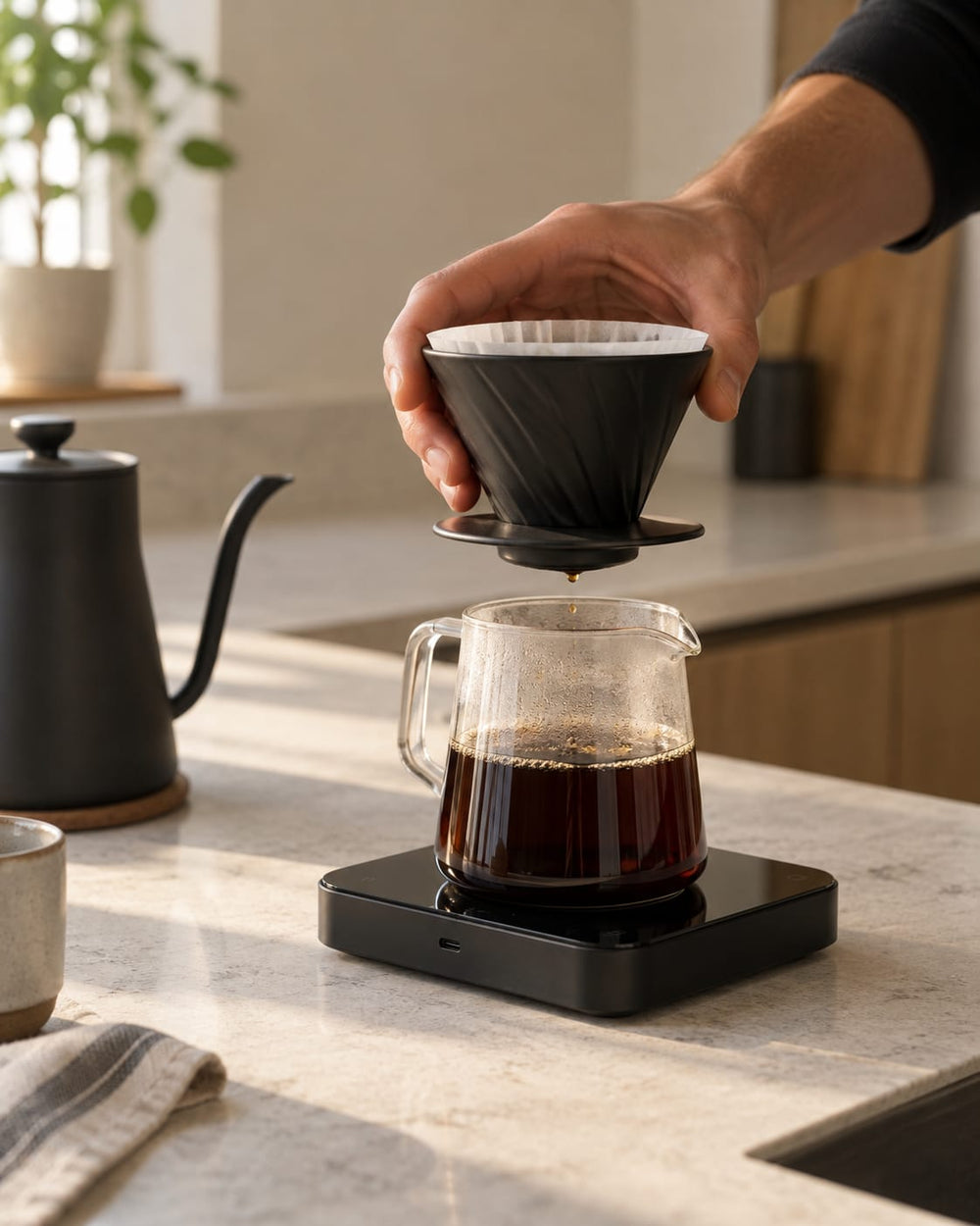 A hand lifting a V60 dripper over a glass server of fresh filter coffee